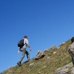 Man with rucksack walking up a hillside against a blue sky